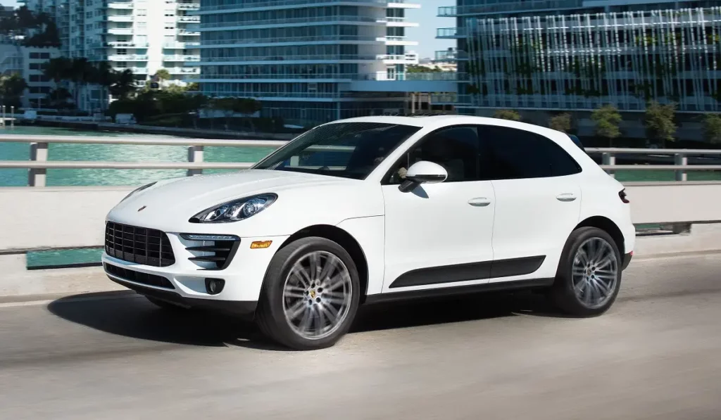 white porsche macan driving with sea and building in background